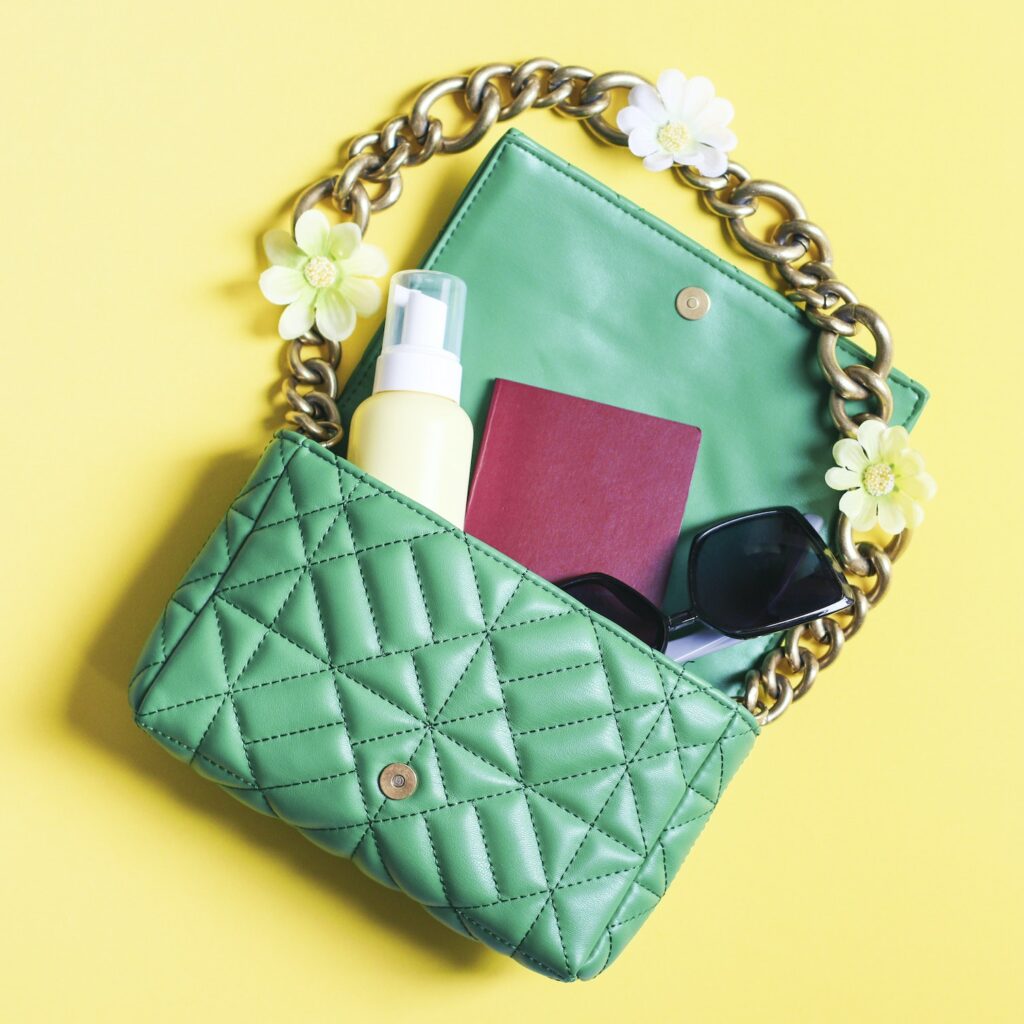 Stylish quilted green handbag, sunglasses, cream and passport on a yellow background.